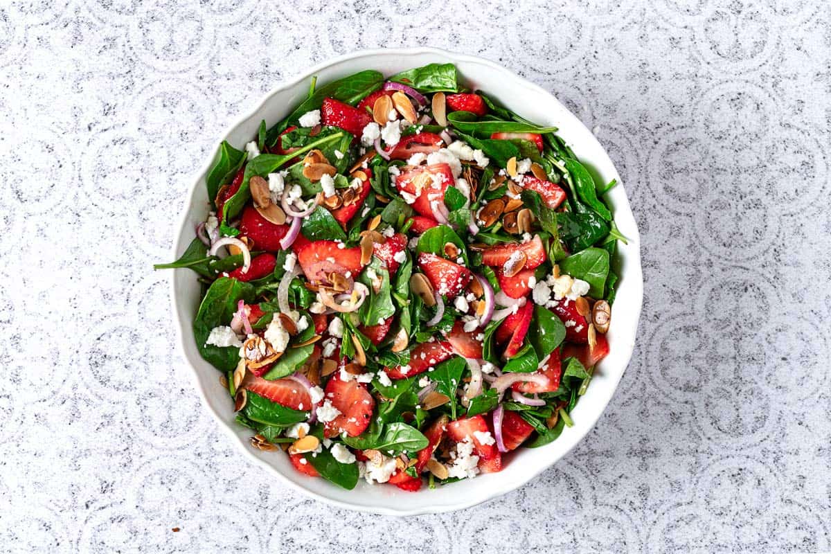 spinach strawberry salad topped with toasted almonds and feta in a bowl.