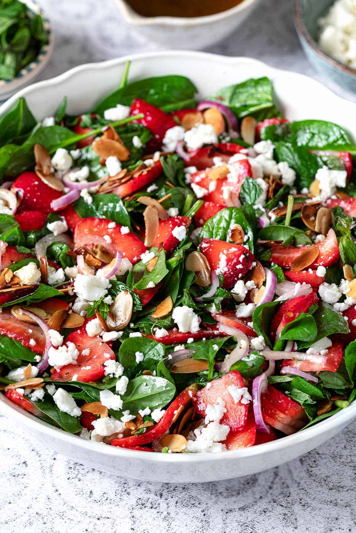 close up of spinach strawberry salad topped with toasted almonds and feta in a bowl.