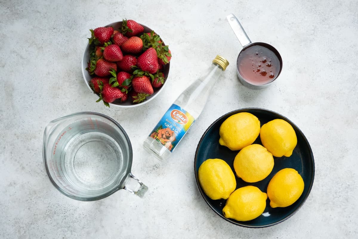 ingredients for strawberry lemonade including strawberries, honey, lemons, water, and rosewater.