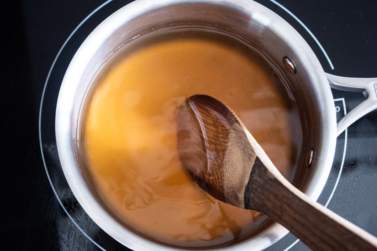 honey syrup being simmered in a saucepan with a wooden spoon.