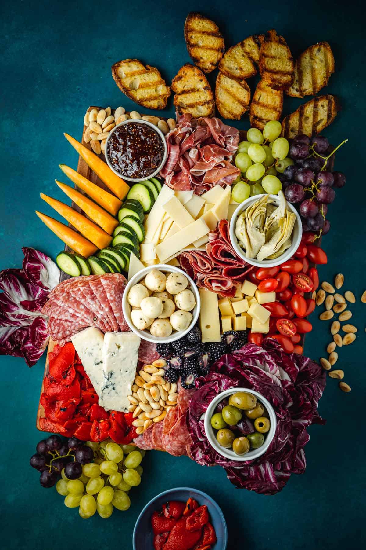 overhead photo of a large antipasto platter with a selection of meats, cheeses, fruits, vegetables, nuts and toasted bread slices.