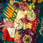 overhead photo of a large antipasto platter with a selection of meats, cheeses, fruits, vegetables, nuts and toasted bread slices.