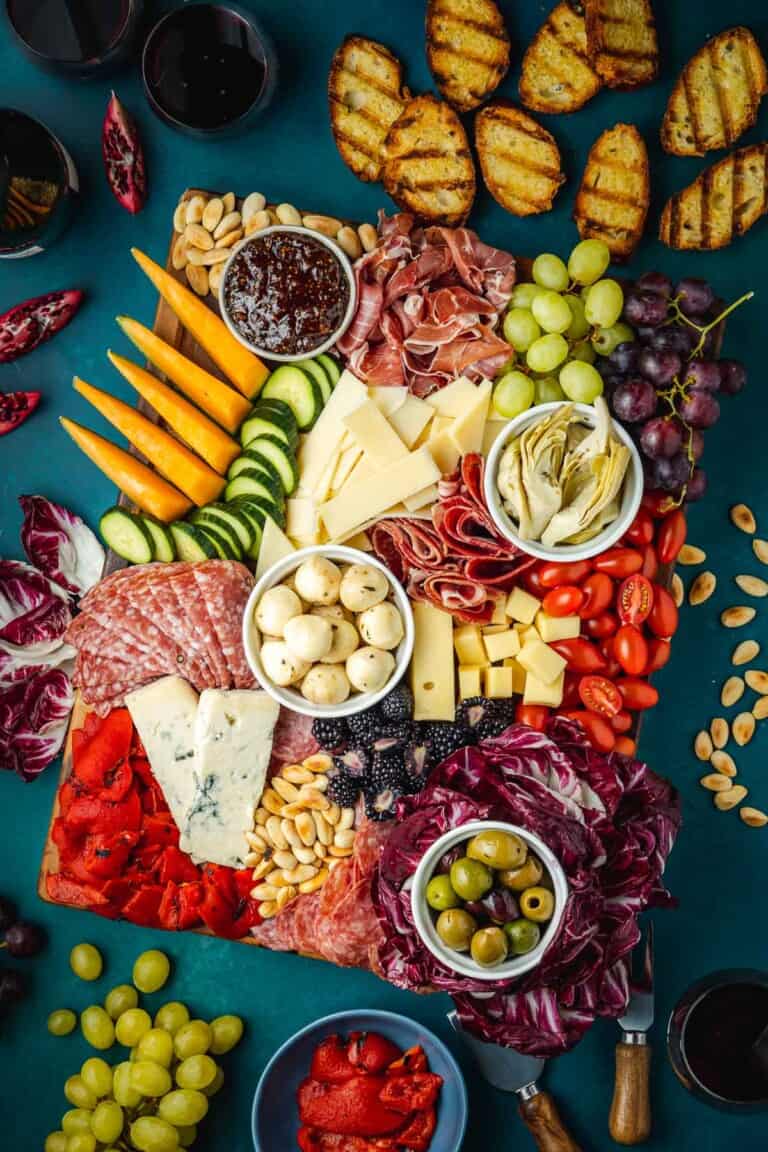 overhead photo of a large antipasto platter with a selection of meats, cheeses, fruits, vegetables, nuts and toasted bread slices.