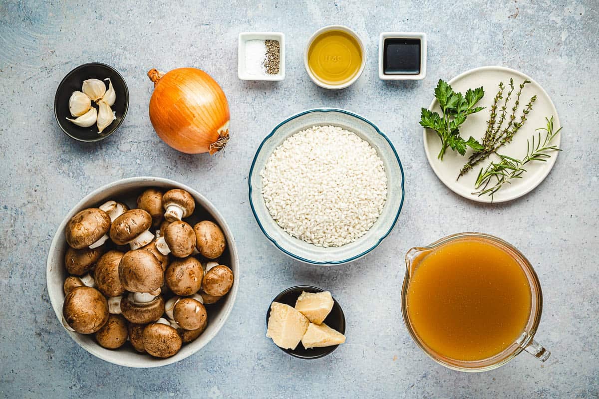 ingredients for mushroom risotto including chicken stock, olive oil, onion, mushrooms, thyme, parsley, rosemary, salt, pepper, garlic, balsamic vinegar, arborio rice, and parmesan cheese.