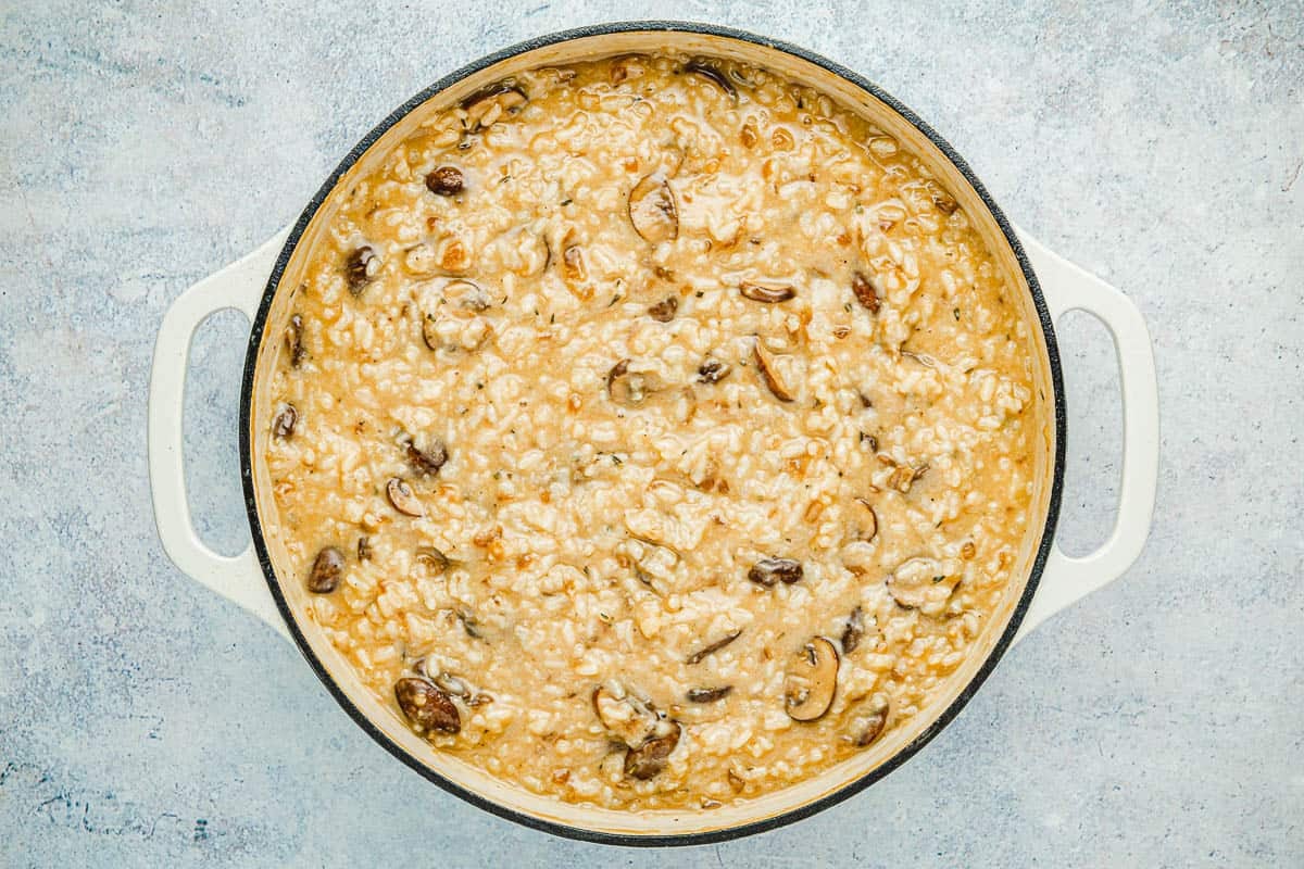 arborio rice and sauteed sliced mushrooms cooking in chicken stock in a skillet.