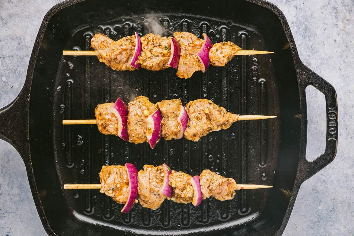 Pork souvlaki skewers that have just been placed on a hot grill pan.