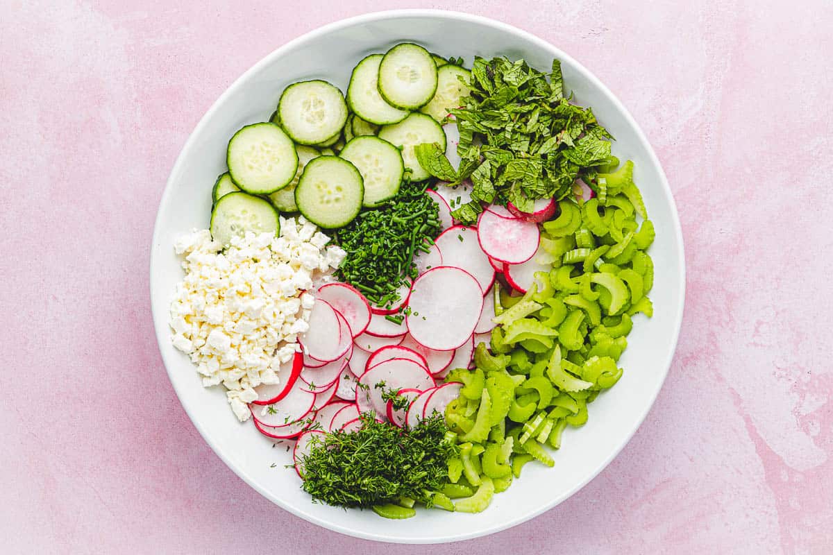 sliced cumber, sliced radishes, sliced celery, minced dill, minced chives, chopped mint and crumbled goat cheese in a bowl before being mixed together.