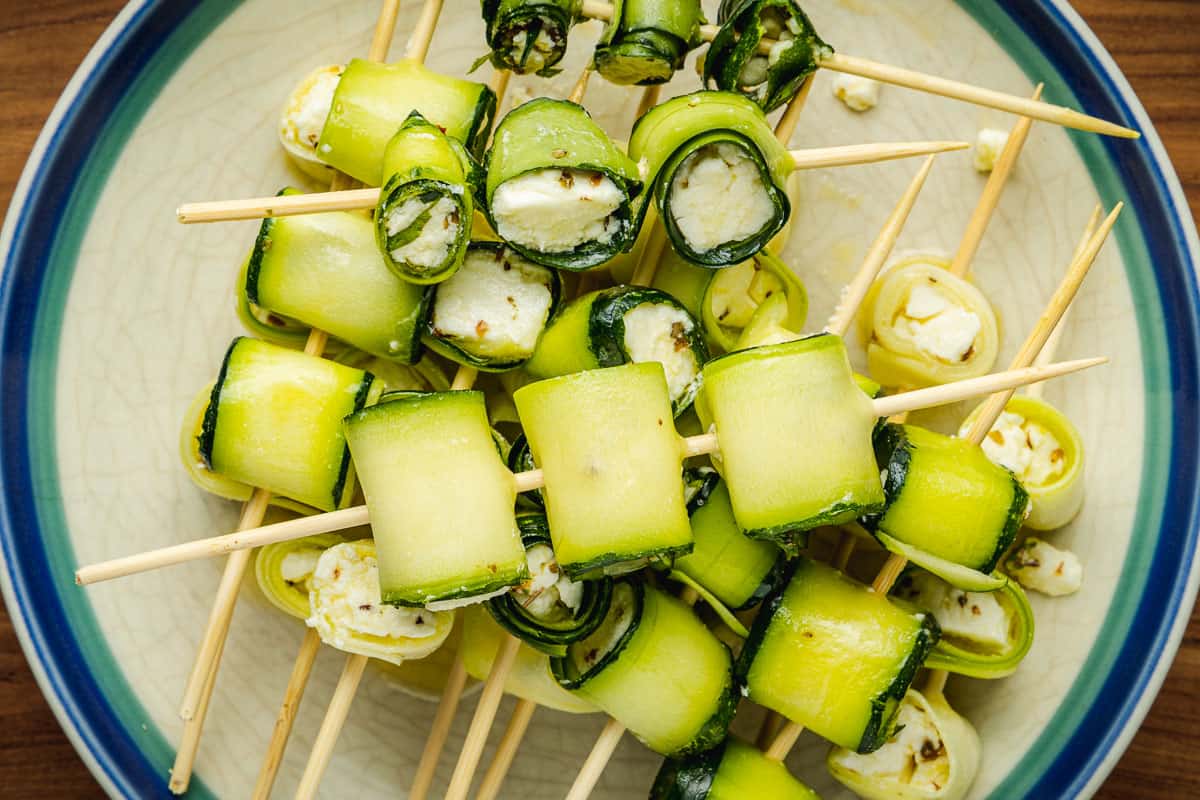 several uncooked zucchini roll up skewers piled on a plate.