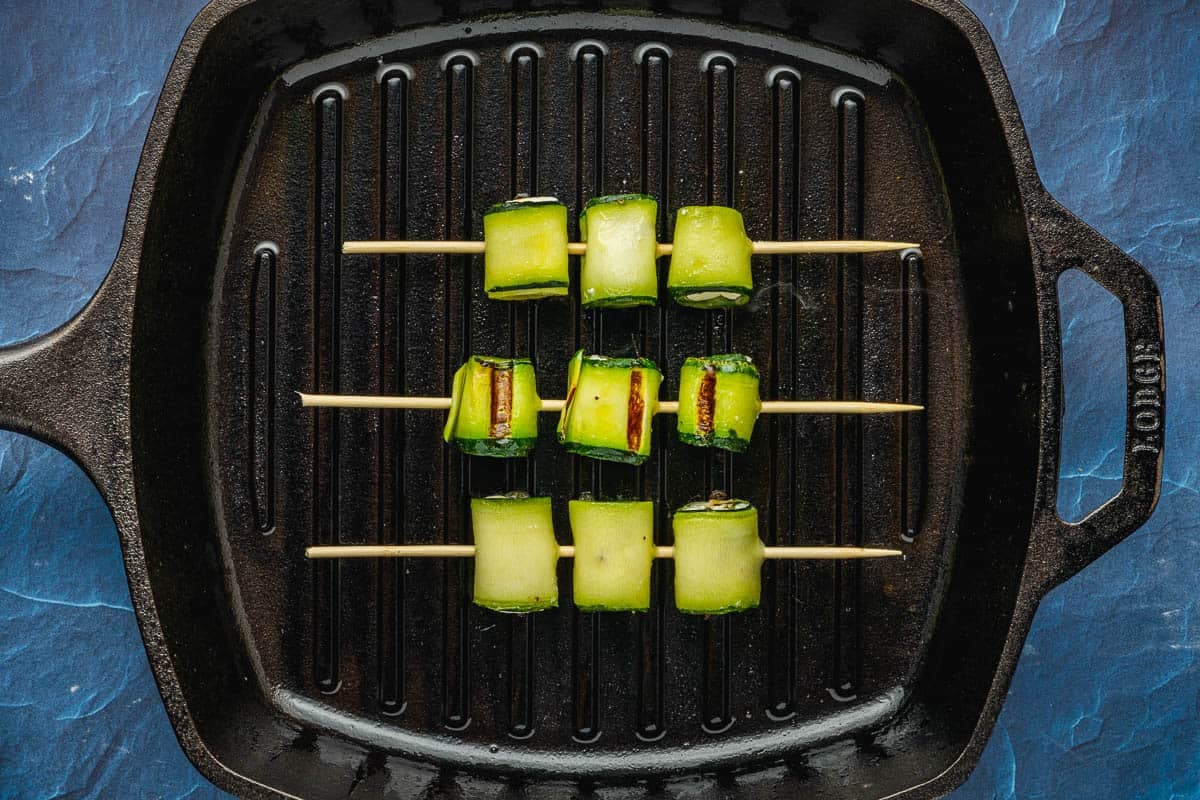 3 zucchini roll up skewers on a cast iron grill pan.
