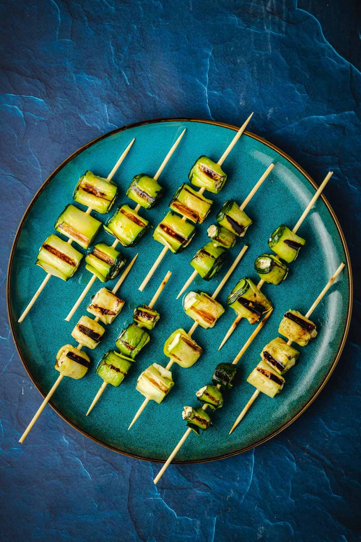 10 grilled zucchini roll up skewers on a plate.