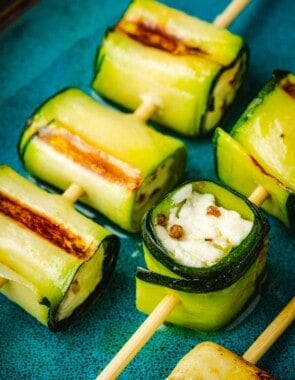 close up of two grilled zucchini roll up skewers on a plate.