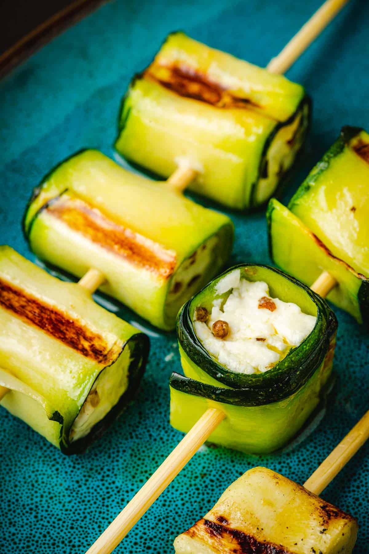close up of two grilled zucchini roll up skewers on a plate.