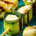 close up of a grilled zucchini roll up skewer on a plate.