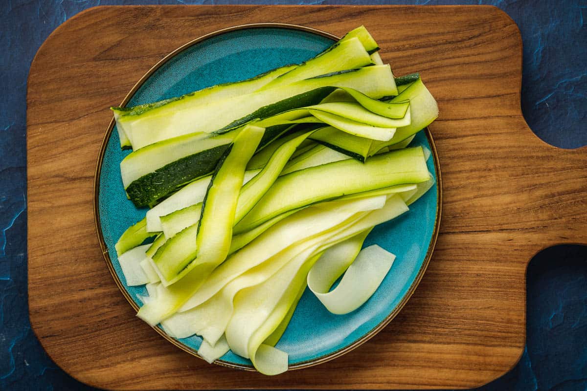 long, thin ribbons of zucchini on a plate, sitting on a wooden tray.