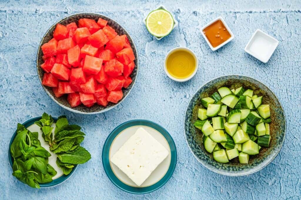 ingredients for watermelon salad including watermelon, lime, olive oil, honey, salt, cucumber, feta, mint and basil.