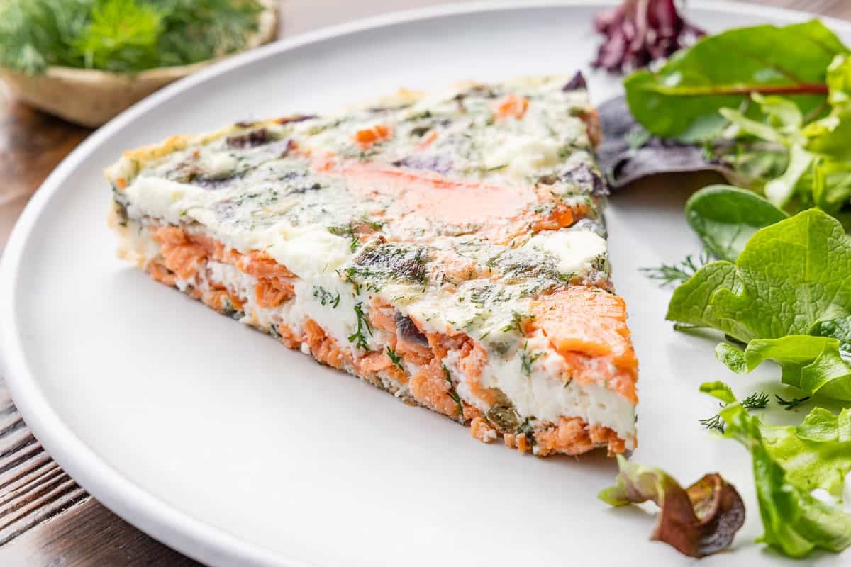 close up of a slice of an egg white frittata on a plate with a small salad.