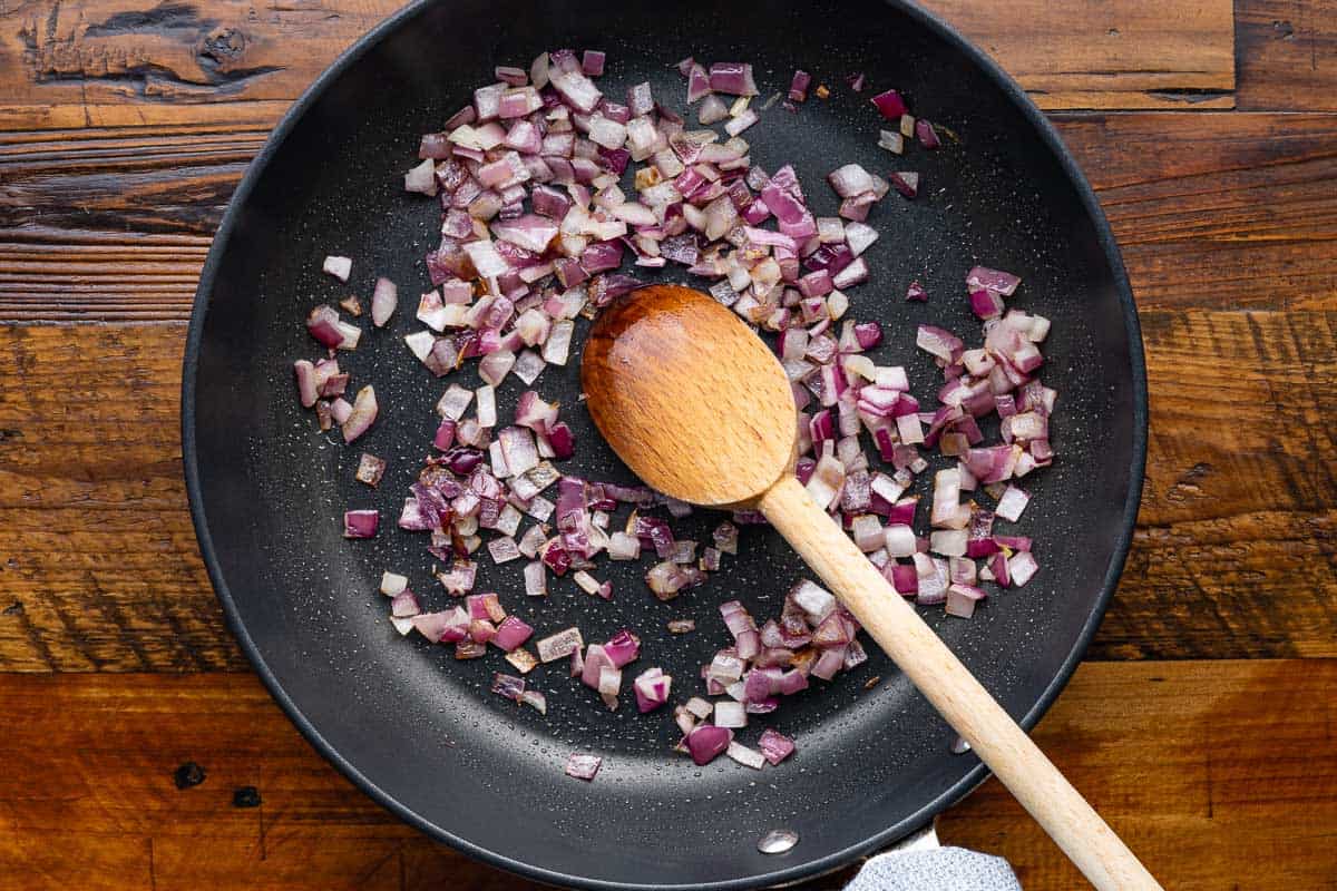 chopped red onions sautéing in a skillet with a wooden spoon.