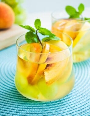 Glass of white wine sangria with sliced peaches and a garnish of fresh mint.