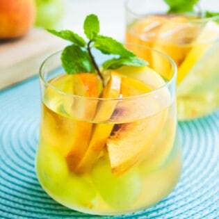 Glass of white wine sangria with sliced peaches and a garnish of fresh mint.