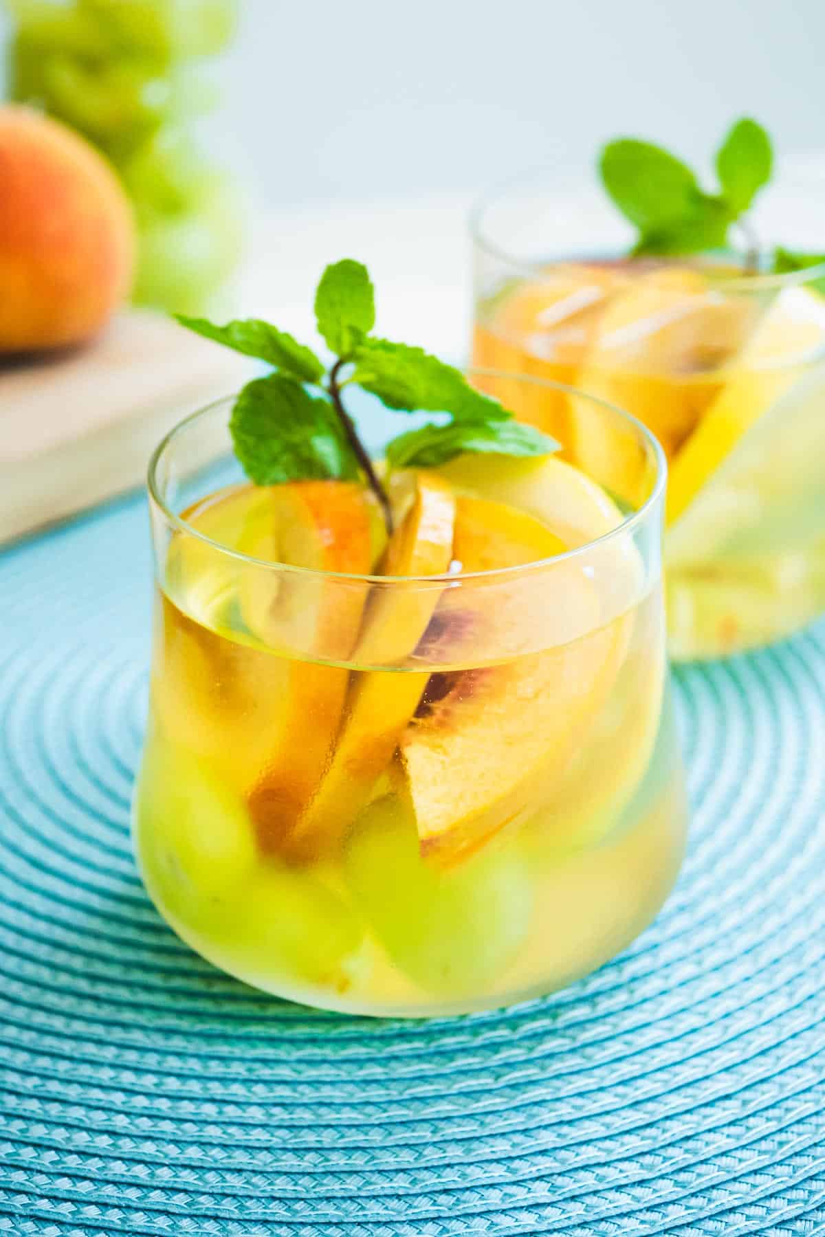 Glass of white wine sangria with sliced peaches and a garnish of fresh mint.