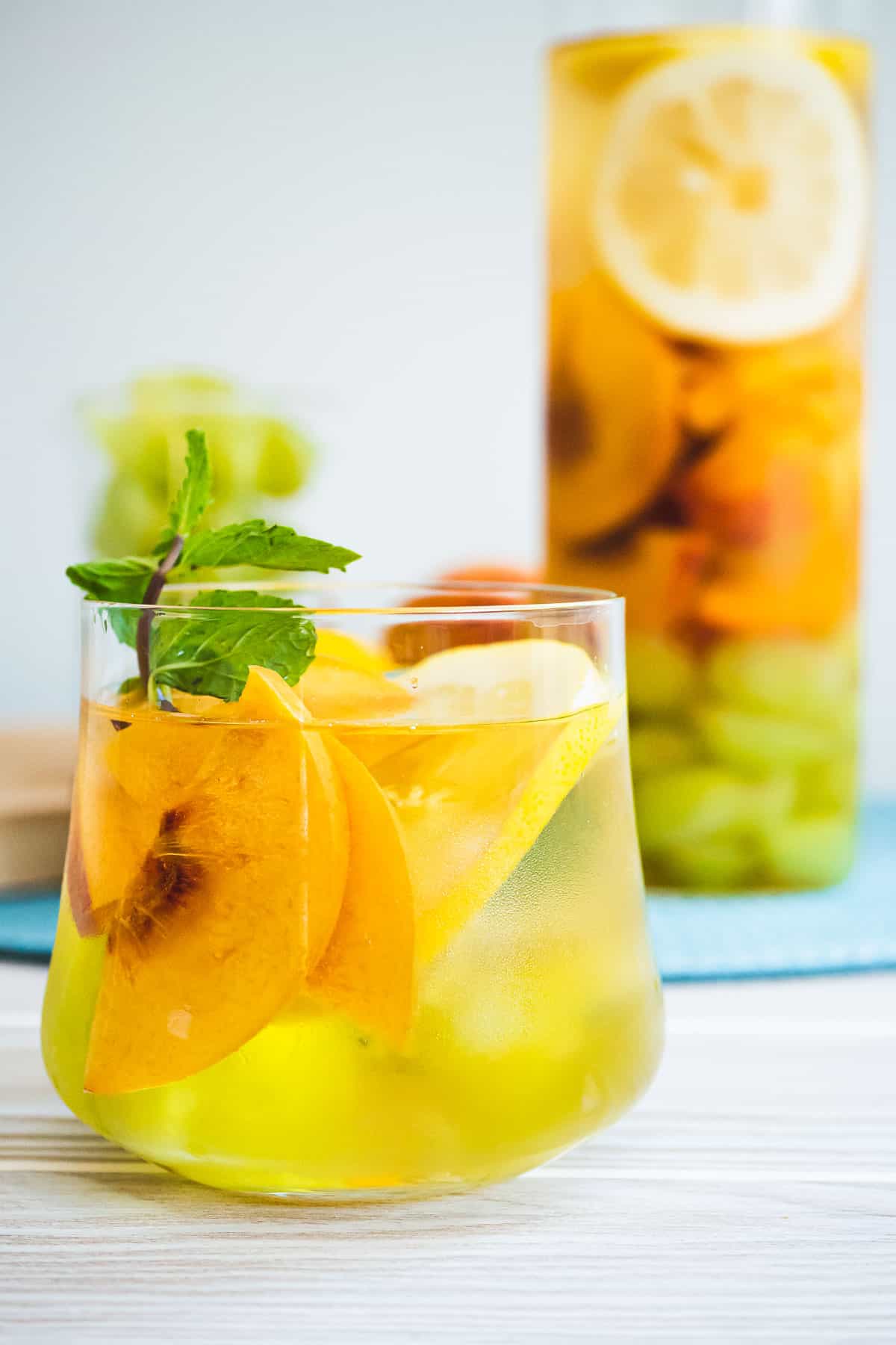 Glass of white wine sangria with sliced yellow peaches, lemon, and a sprig of fresh mint.