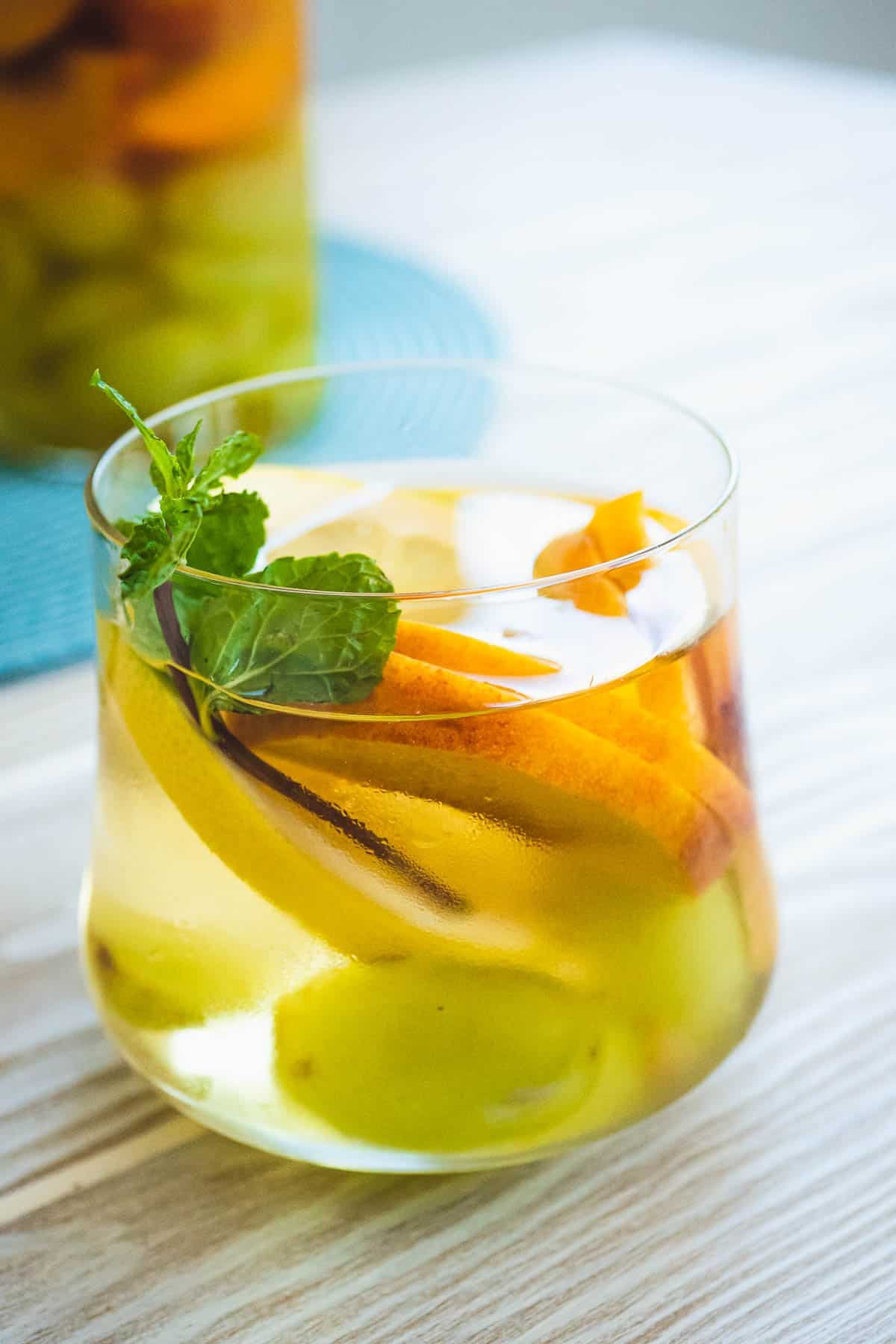 Glass of cold white wine sangria with green grapes, yellow peaches, lemon, and mint.