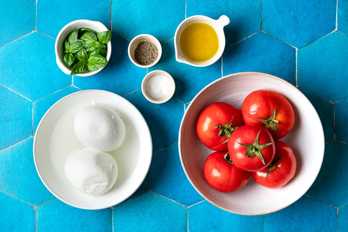 ingredients for caprese salad including tomatoes, mozzarella, basil, salt, pepper, and olive oil.
