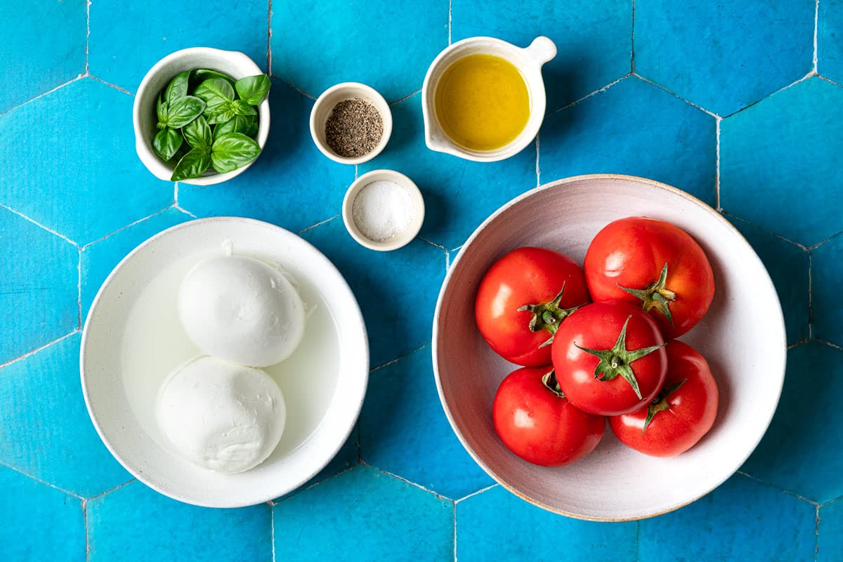ingrédients pour la salade caprese, notamment tomates, mozzarella, basilic, sel, poivre et huile d'olive.