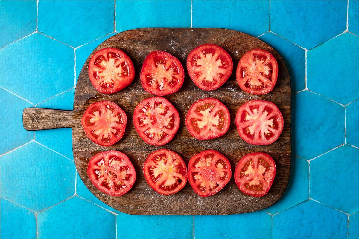 12 tranches de tomates sur une planche à découper.