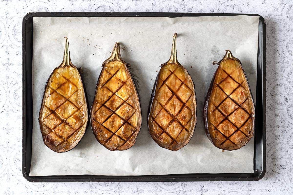 Four roast eggplant halves on a sheet tray.