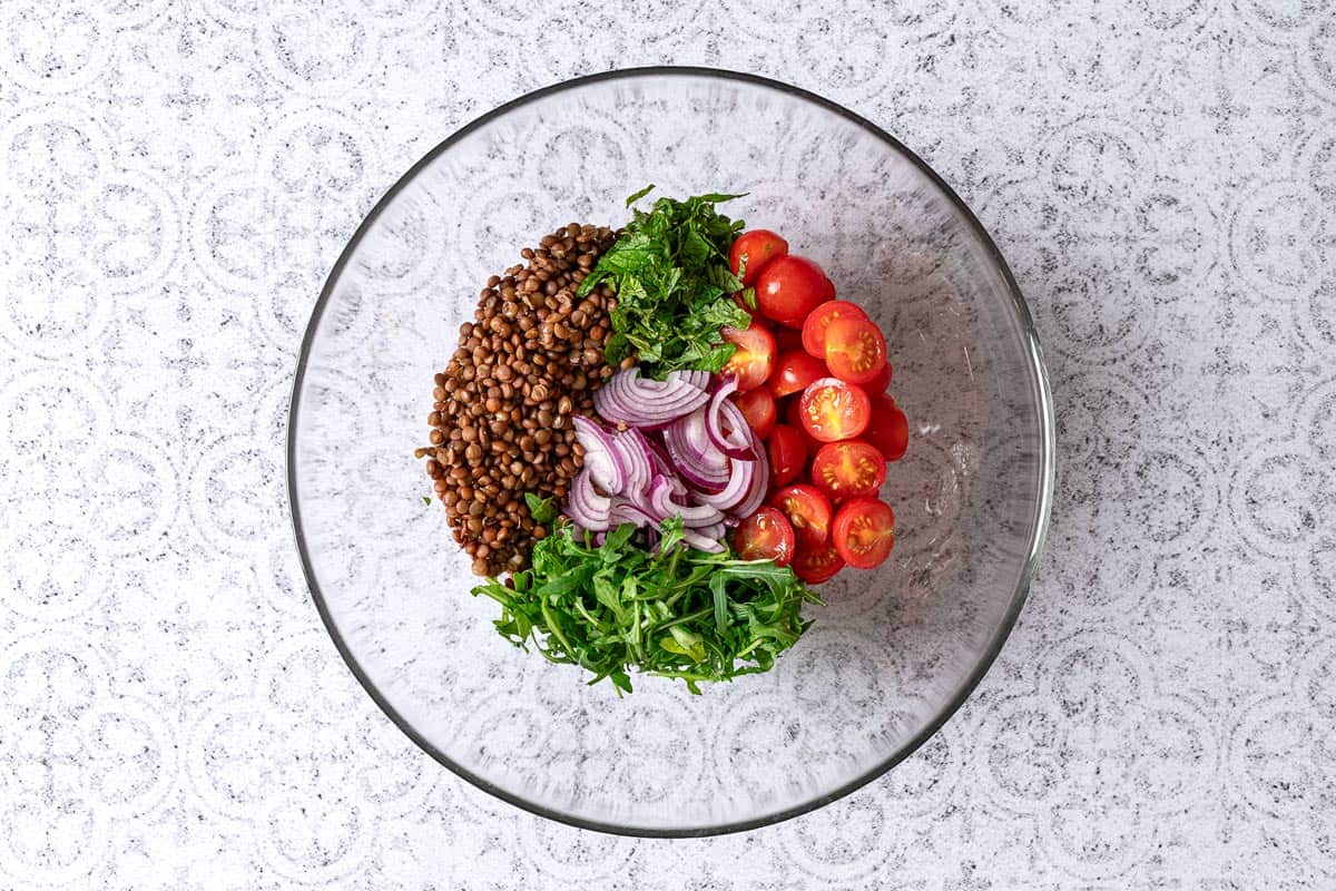 Herbs, arugula, cherry tomatoes, and lentils in a glass mixing bowl.