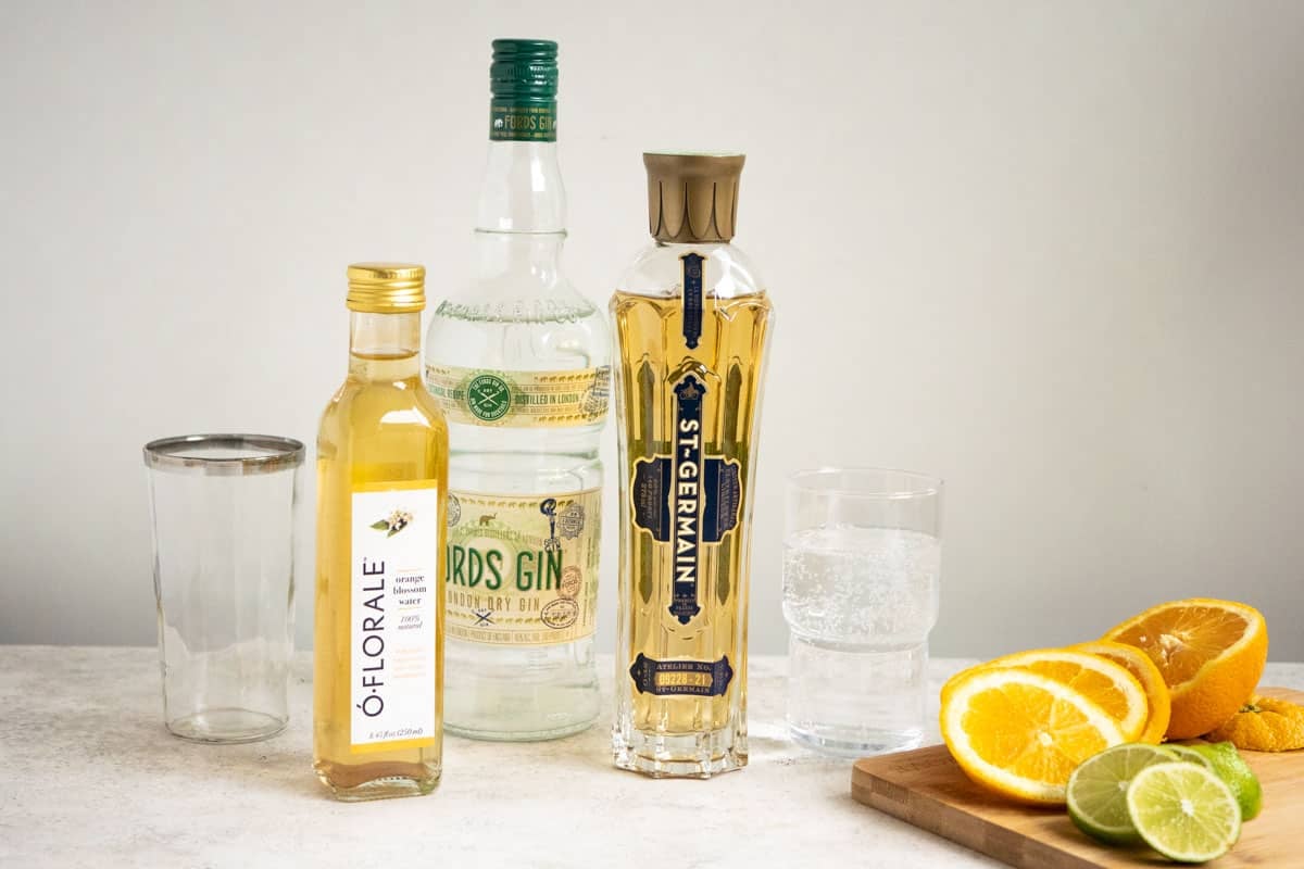 ingredients for eternal sunshine gin cocktail including orange blossom water, gin, st. Germain elderflower liqueur, tonic, lime and orange.