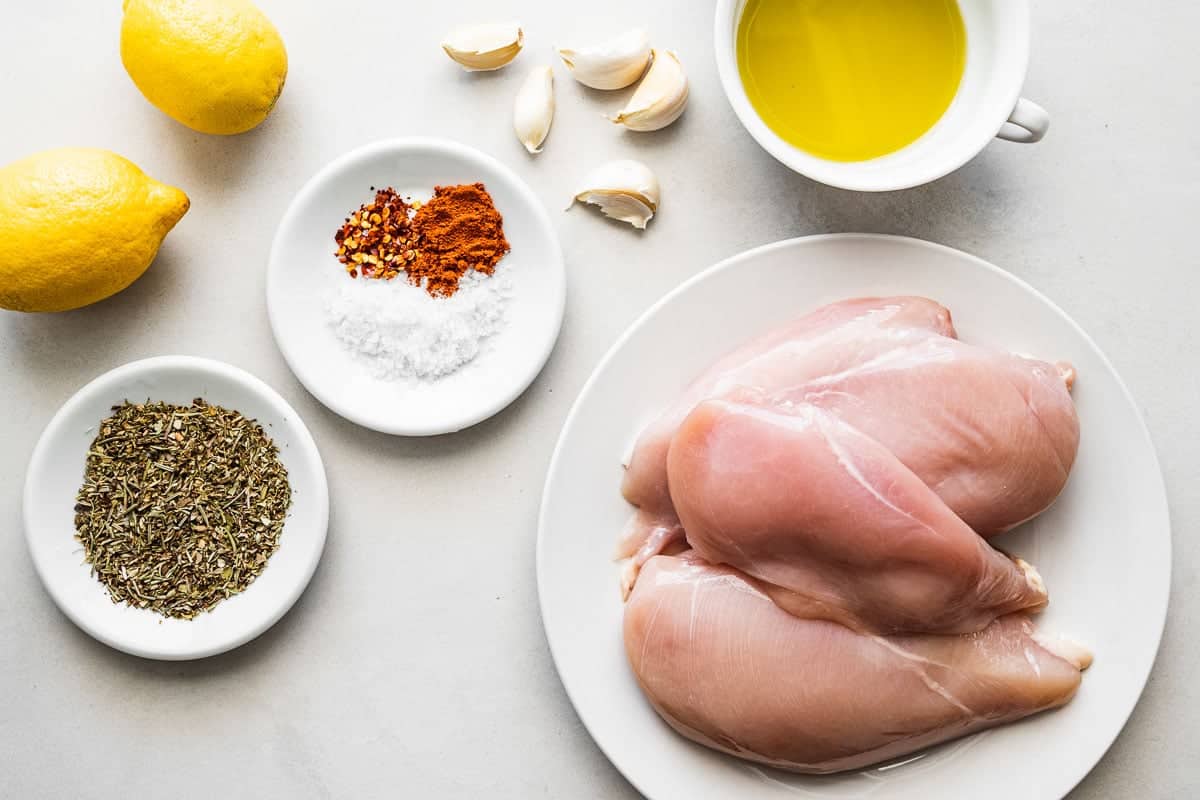 ingredients for grilled chicken breast including chicken, olive oil, garlic, italian seasoning, paprika, red pepper flakes, salt and lemons.