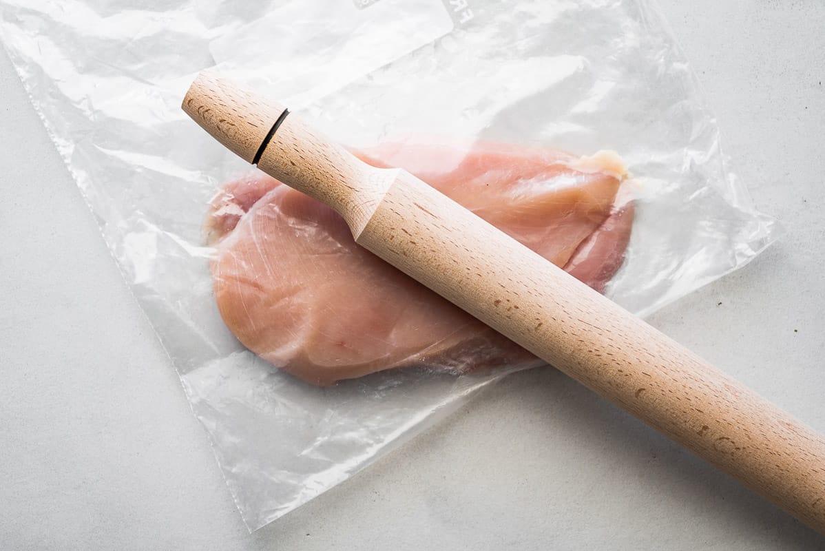 a raw chicken breast in a plastic bag with a rolling pin sitting on top.