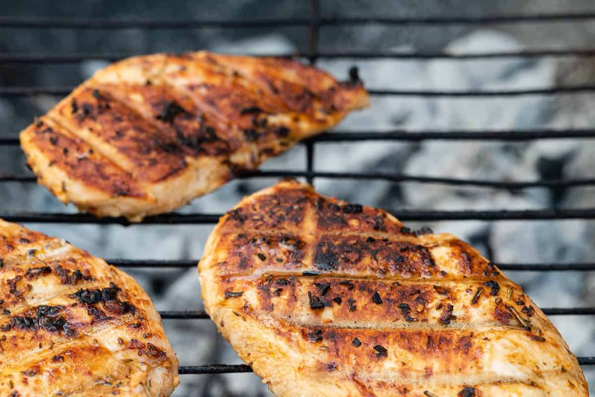 3 chicken breasts grilling on a grill.
