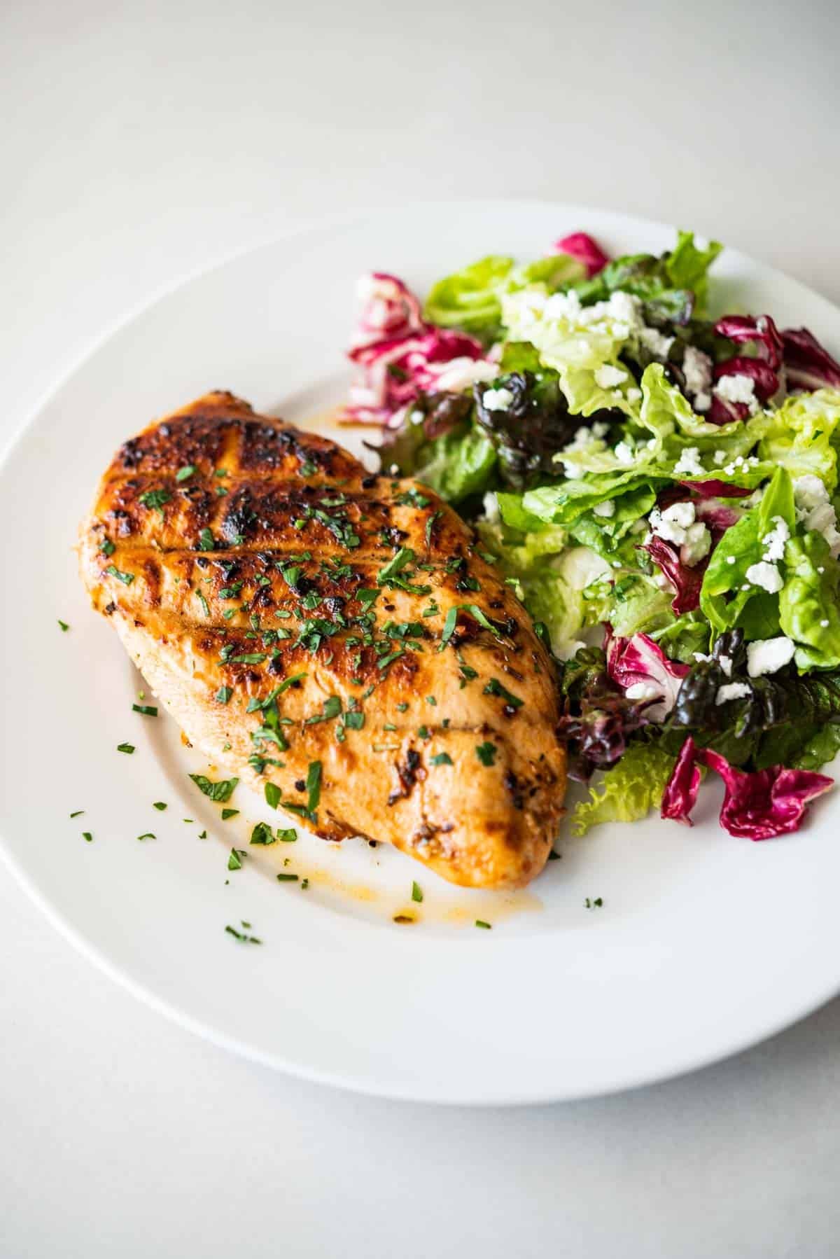 a grilled chicken breast with a salad on a plate.