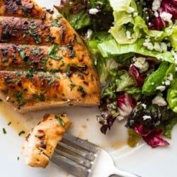 a grilled chicken breast with a piece of it on a fork and a salad on a plate.