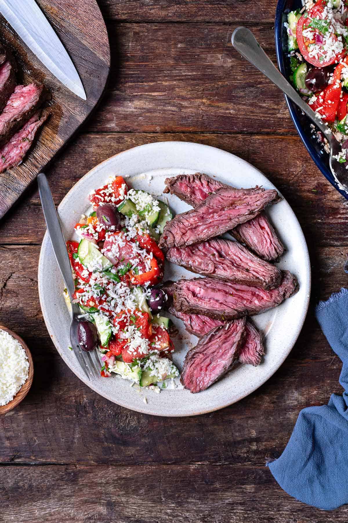 overhead photo of grilled skirt steak slices on a plate with a side of shopska salad and a fork.