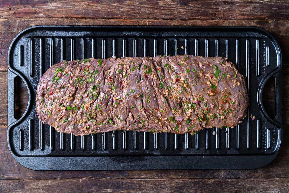 uncooked marinated skirt steak on a cast iron grill pan.