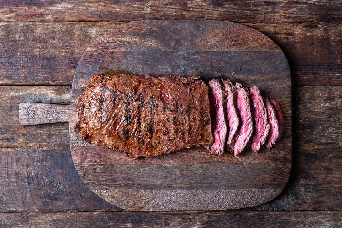 a half-sliced grilled skirt steak on a cutting board.