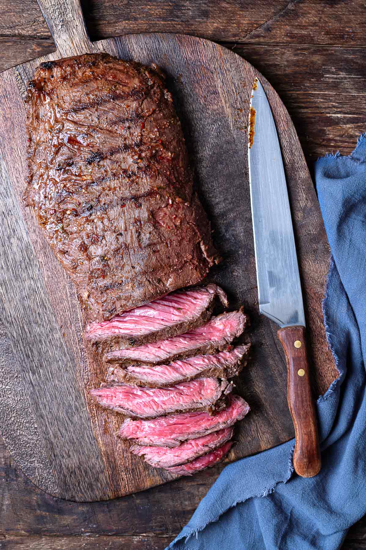 a half-sliced grilled skirt steak on a wooden cutting board with a knife.