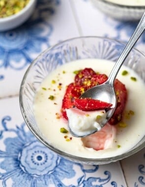 a bite of Rose Mahalabia (Milk Pudding) topped with strawberries and pistachios being lifted out of a bowl with a spoon.
