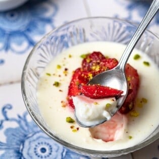a bite of Rose Mahalabia (Milk Pudding) topped with strawberries and pistachios being lifted out of a bowl with a spoon.