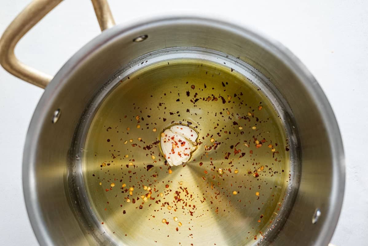 garlic and red pepper flakes simmering in olive oil in a pot.