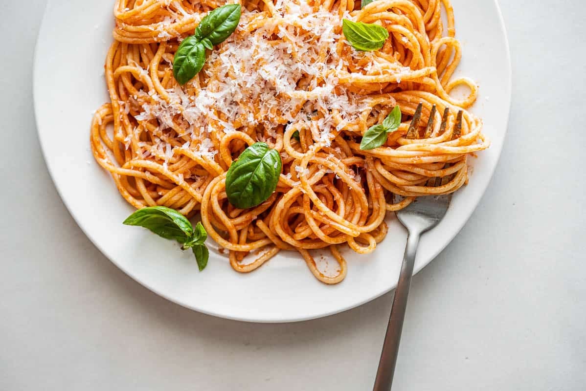 one plate of pasta pomodoro topped with grated parmesan and basil with a fork.