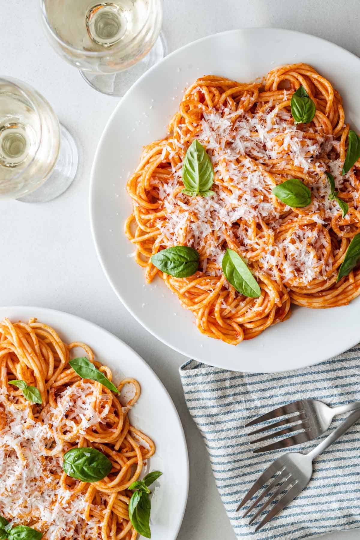 overhead photo of two plates of pasta pomodoro topped with grated parmesan and basil next to two forks, a napkin and two glasses of white wine.