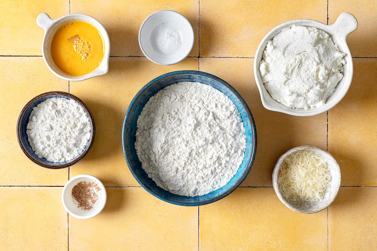 ingredients for ricotta gnocchi including flour, ricotta, Parmigiano-Reggiano cheese, a lightly beaten egg, salt and nutmeg.