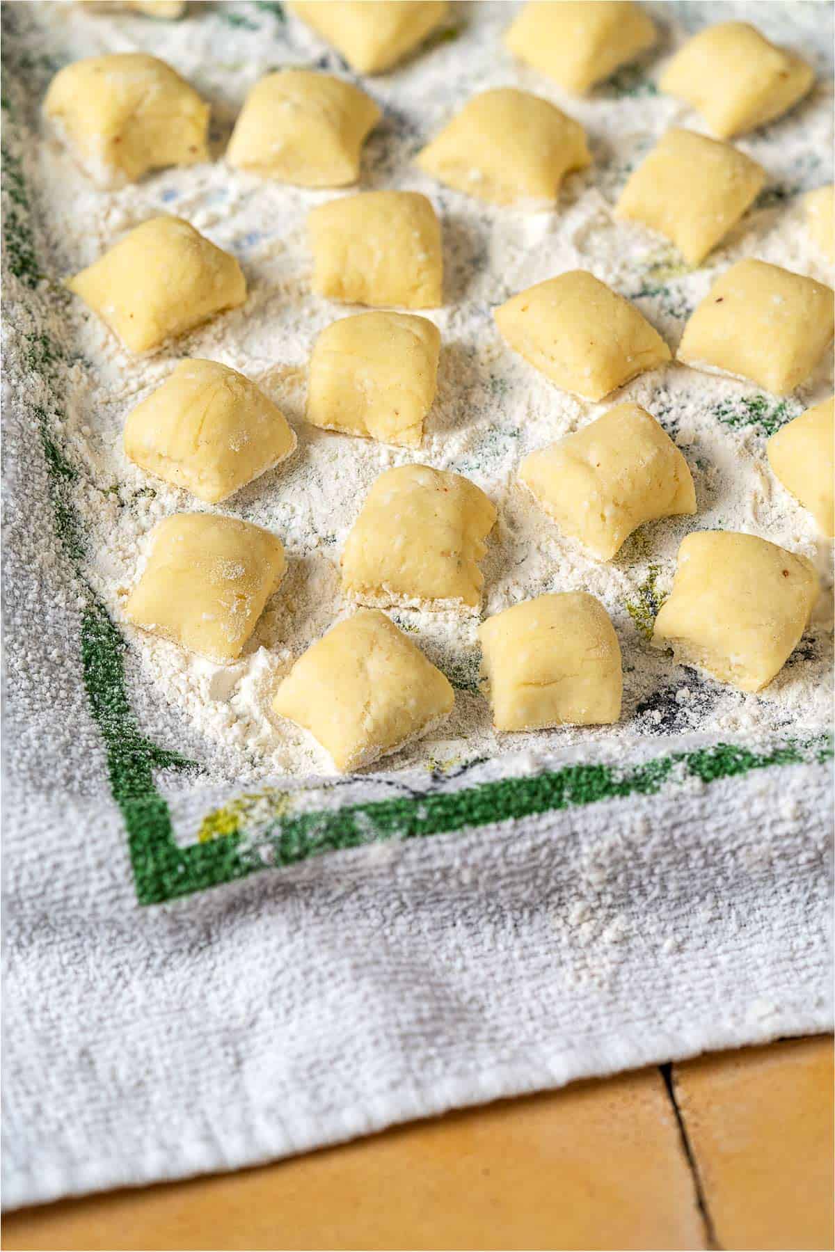 a close up of ricotta gnocchi pieces on a towel sprinkled with flour.