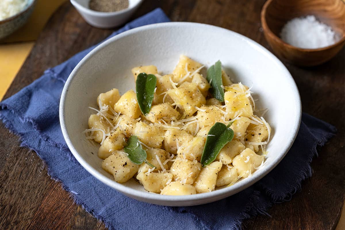 a bowl of cooked ricotta gnocchi toped with a sprinkle of parmesan and fresh basil.