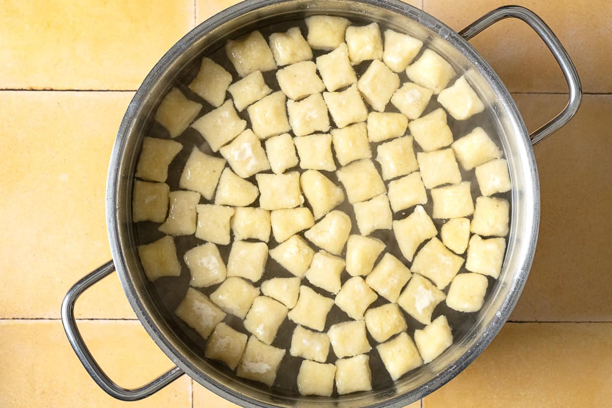 pieces of ricotta gnocchi cooking in water in a large pot.